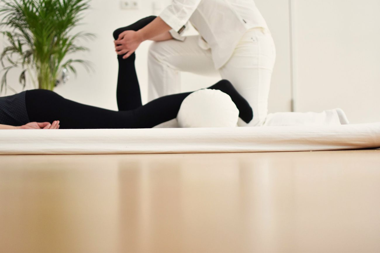 Behandlung auf der Matte: ein Bein wird sanft gelagert, daneben Polster und Zimmerpflanze